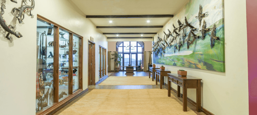 Elegant hallway with wooden accents, display cabinets featuring decorative art pieces, large bird-themed wall artwork, and bright natural light streaming through tall windows at t…