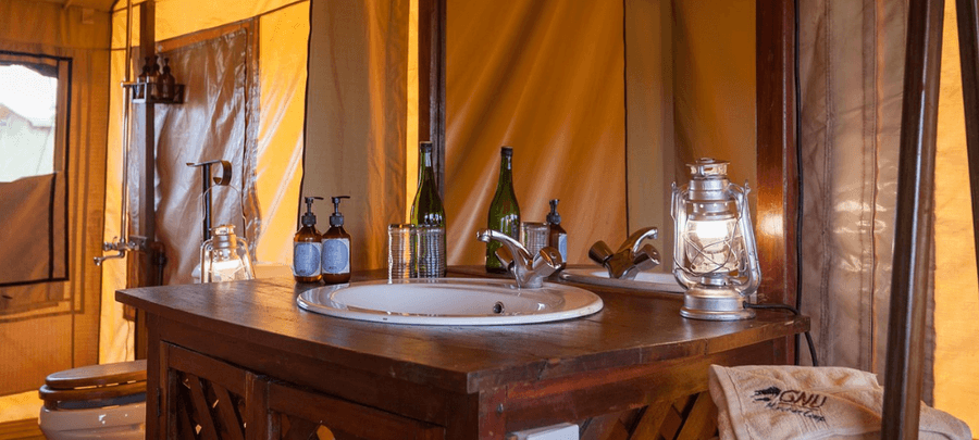 Safari tent bathroom at GNU Camp with wooden vanity, sink, lantern lighting, and eco-friendly amenities in a canvas setting