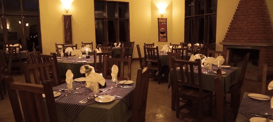 Warm and inviting restaurant dining area with neatly set wooden tables and chairs, soft ambient lighting, and a large brick fireplace creating a cozy atmosphere.