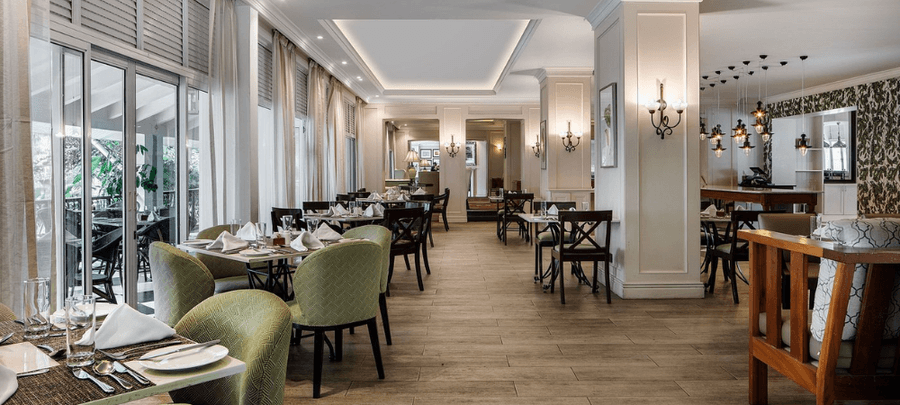Elegant hotel restaurant with neatly set dining tables, cushioned chairs, warm lighting, large windows, and a spacious modern interior with soft neutral décor.