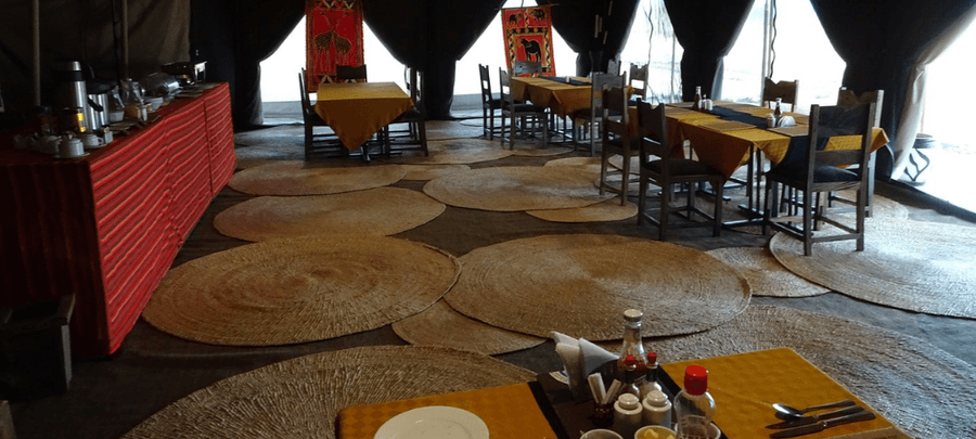 Safari dining tent with wooden tables, woven circular rugs, and warm African-inspired décor creating a cozy and inviting dining atmosphere.