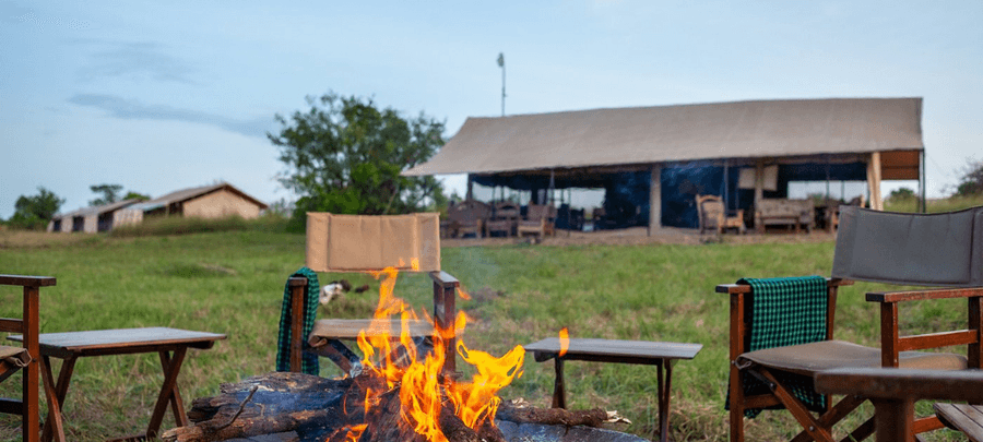 Campfire seating area with safari chairs at GNU Camp, overlooking open grassland and a main lodge in the background at dusk