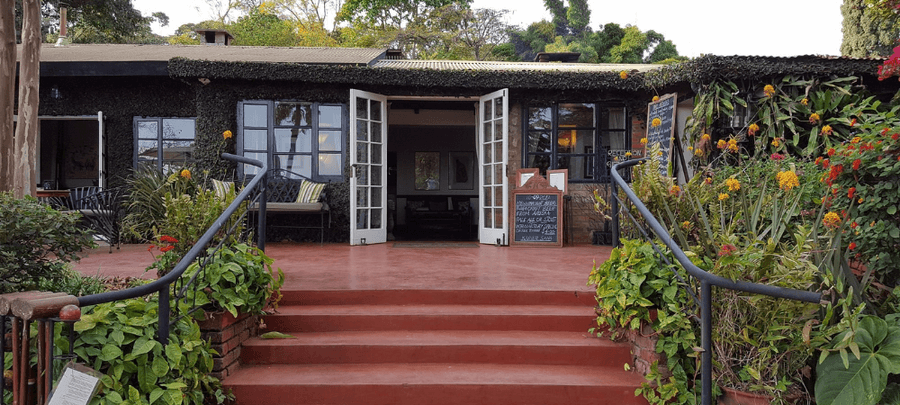 Inviting garden-front lodge entrance with open French doors, terracotta steps, lush flowering plants, and cozy outdoor seating surrounded by greenery.