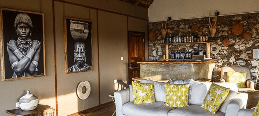 Cozy safari lodge lounge with African artwork, a stone bar, and comfortable seating, blending rustic charm with modern comfort.