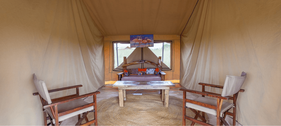 Comfortable lounge area inside a safari tent at GNU Camp with wooden chairs, a coffee table, and a cozy seating space overlooking the savannah