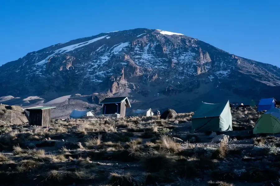 Campsite at the base of Mount Kilimanjaro with tents and snow-capped slopes under a clear sky.