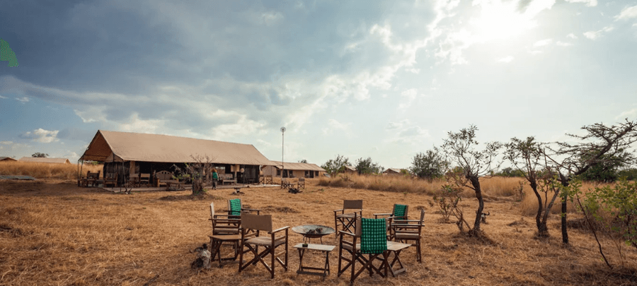 GNU Camp safari tented lodge set in open savannah, with outdoor chairs around a fire pit and main tent under a partly cloudy sky.